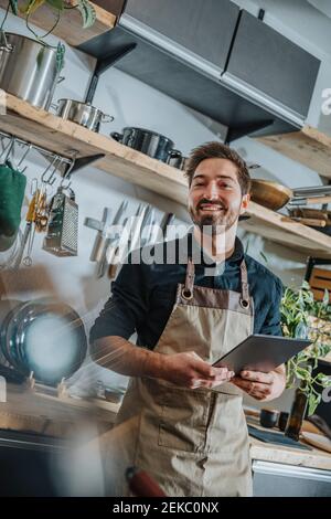Lächelnder Chefkoch mit digitalem Tablet, während er in der Küche steht Stockfoto