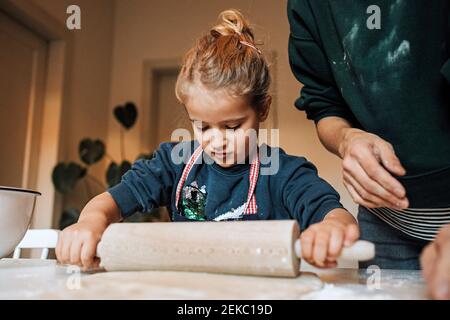 Mädchen hilft ihrer Mutter mit rollenden Teig für Zimtrollen In der Küche Stockfoto