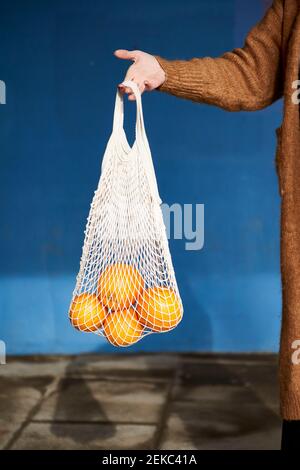Frau hält Orangen im wiederverwendbaren Beutel an der Wand auf dem Fußweg Stockfoto