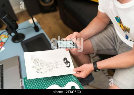 Künstler, der während des Sitzens ein Designfoto über das Mobiltelefon gemacht hat Zu Hause Stockfoto