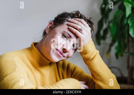 Lächelnde Frau mit dem Kopf in den Händen starrend, während sie ansitzt Zu Hause Stockfoto