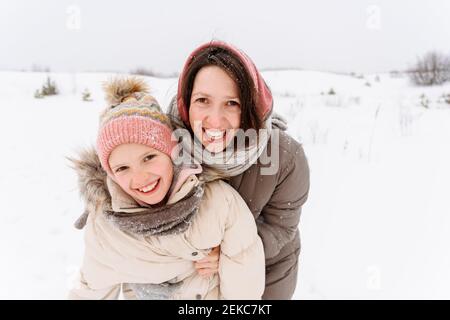 Lächelnde Mutter mit Tochter, die auf verschneite Landschaft steht Stockfoto