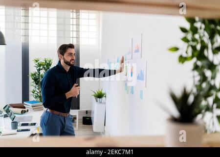 Männlicher Unternehmer, der Strategien betrachtet, während er im Büro steht Stockfoto