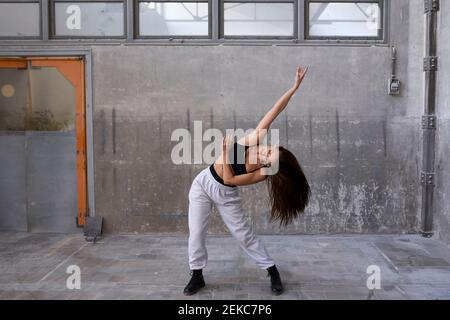 Tänzerin, die in einer verlassenen Fabrik gegen die Wand übt Stockfoto