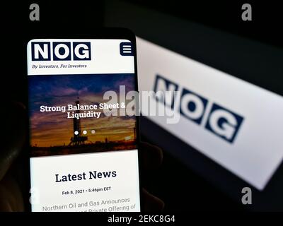 Person, die Mobiltelefon mit der Webseite des US-Ölunternehmens Northern Oil and Gas (NOG) auf dem Bildschirm vor dem Logo hält. Fokus auf der Mitte des Telefondisplays. Stockfoto