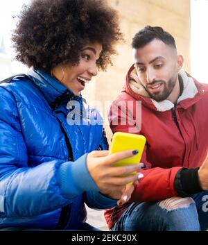 Aufgeregt Frau zeigt Handy an Freund, während im Freien sitzen Stockfoto