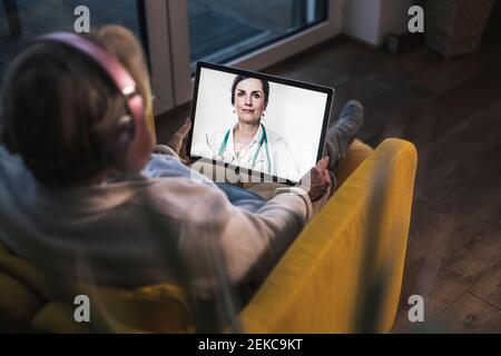 Ältere Frau auf Videoanruf mit Ärztin durch digital Tablet im dunklen Raum Stockfoto