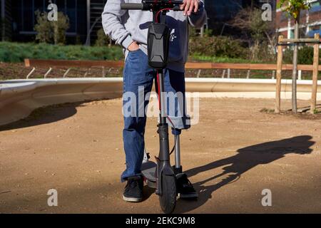 Junger behinderter Mann mit der Hand in der Tasche, die bei einem Elektromotor steht Roller auf dem Spielplatz schieben Stockfoto