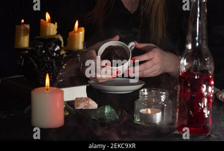 Wahrsagerei auf Kaffeesatz. Die Hände eines Wahrsager, eine Tasse Kaffee, Kerzen und Schädel auf einem schwarzen Tisch. Das Konzept der Zauberer, Hexerei Stockfoto