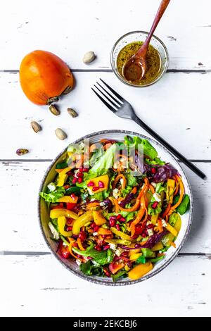 Gemischter Salat mit Paprika, Feta, Pistazien, Tomaten, Granatapfelkernen, Kaki und Dressing Stockfoto