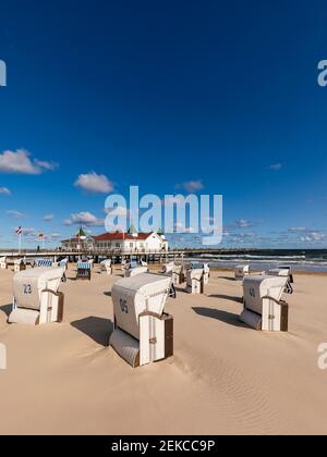 Deutschland, Mecklenburg-Vorpommern, Heringsdorf, Kapuzenliegen am leeren Strand mit Ahlbeck Pier im Hintergrund Stockfoto