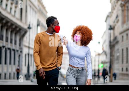 Junge Frau trägt schützende Gesichtsmaske Blick auf Mann, während Zu Fuß in der Stadt