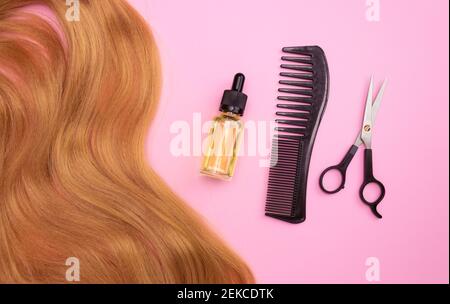 Braunes Kunsthaar auf rosa Hintergrund, kosmetisches Öl in einer Glasflasche mit Pipette, Kamm und Schere. Das Konzept eines Friseursalons, Haarschnitt Stockfoto