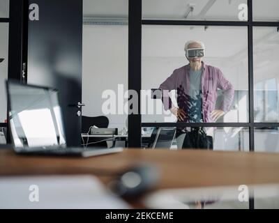 Leitender Geschäftsmann, der im Büro mit einem Virtual-Reality-Headset steht Stockfoto