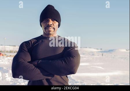 Muskulös bauen Sportler tragen Strickmütze stehen mit Armen gekreuzt Im Schnee an sonnigen Tagen Stockfoto