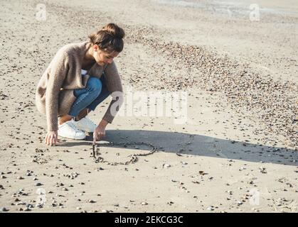 Junge Frau zieht Herz auf Sand am Strand Stockfoto