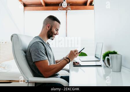 Lächelnder junger Mann, der an Laptop und Handy arbeitet Zu Hause Stockfoto
