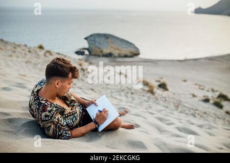 Junger Mann auf Sanddüne beim Zeichnen in Buch in Almeria, Wüste Tabernas, Spanien Stockfoto