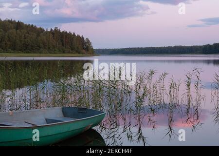 Schöner Sonnenuntergang Blick auf den See mit symmetrischen Reflexionen im Wasser von rosa Wolken und ein Fischerboot am Ufer Stockfoto