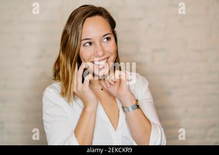 Lächelnde Geschäftsfrau, die über das Mobiltelefon gegen die Wand spricht Stockfoto