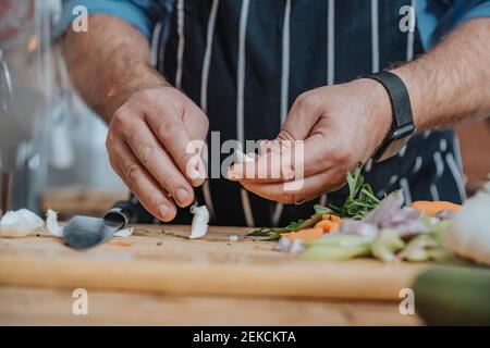 Männlicher Koch trägt Schürze schälen Knoblauch während der Vorbereitung stehen In der Küche Stockfoto