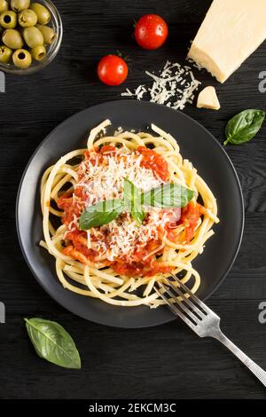 Italienische Pasta mit Tomatensauce und Parmesan auf dem schwarzen Teller auf dem dunklen Holzhintergrund. Draufsicht. Position vertikal. Stockfoto