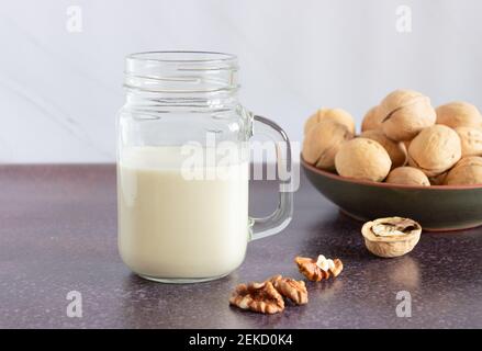 Pflanzliche Walnussmilch in einer Glasschale mit einem Griff. Walnüsse in einer Platte im Hintergrund. Gesunde Getränke, Vegetarismus. Seitenansicht. Stockfoto