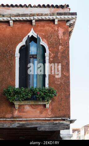 Ein schönes gotisches Fenster mit offenen Fensterläden und einem Fensterkasten in einem alten Terrakotta-Gebäude auf der Insel Murano, Venedig, Italien Stockfoto