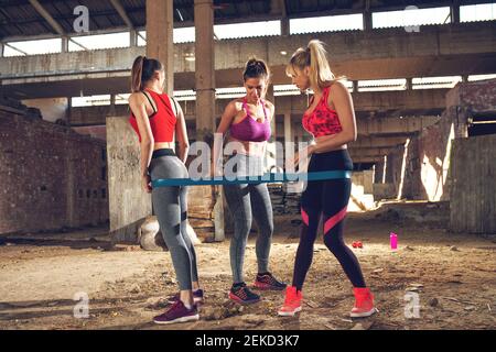 Drei sportlich schlanke Mädels trainieren mit dem Gummiband an der verlassenen Stelle. Stockfoto
