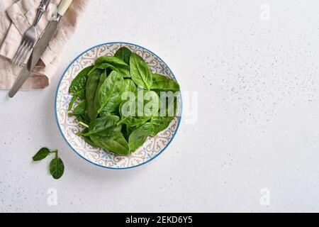Frisches Baby Spinat Blätter in Keramik schöne Schüssel auf hellgrauem Beton Hintergrund. Modell. Draufsicht. Stockfoto