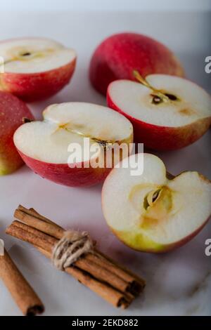 Ganze und in Scheiben geschnittene frische Äpfel mit Zimtstangen auf Marmorboden. Stockfoto