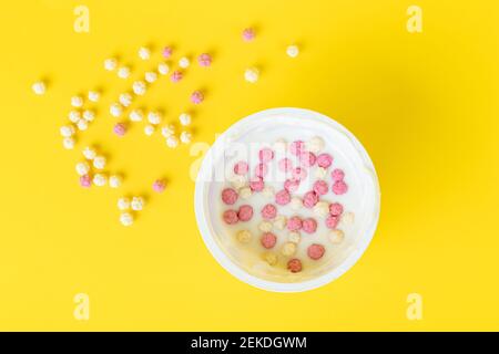 Joghurt in einem Plastikbecher mit knusprigen Flocken, Müsli. Draufsicht. Gelber Hintergrund. Morgen, Frühstückskonzept Stockfoto