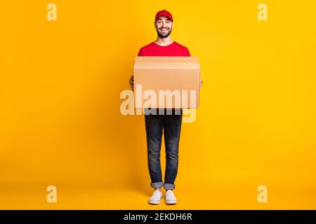 Volle Länge Körpergröße Ansicht der schönen fröhlichen Kerl Mailman Halten in den Händen bringen große Paket schnelle Lieferung isoliert über Lebhaft gelber Hintergrund Stockfoto