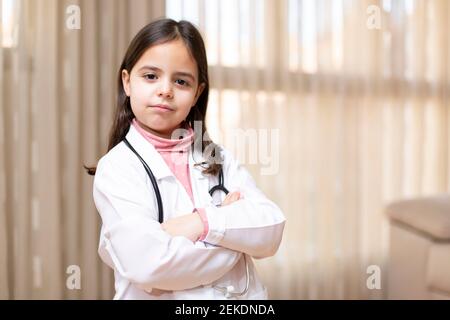 Porträt des kleinen Kindes in Arztuniform posiert mit gekreuzten Armen und verantwortungsvoller Haltung. Konzept von Medizin und Gesundheit. Leerzeichen für Text. Stockfoto