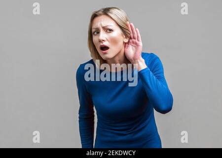 Ich kann es nicht hören! Porträt der neugierigen aufmerksamen Frau in blauem Kleid stehen mit offenem Mund, die Hand in der Nähe des Ohrs und sorgfältig zuhören, um Geheimnis. ind Stockfoto