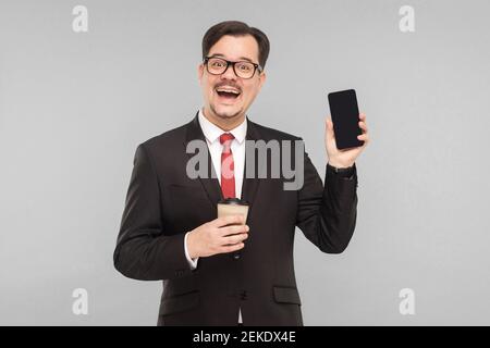 Business, Gadgets, Technologien. Mann zeigt neues Telefon. Indoor, Studioaufnahme, isoliert auf grauem Hintergrund Stockfoto