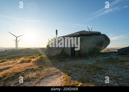 Schönes Stein Penedo Boulder House in Fafe, in Portugal mit eolischen Turbinen im Hintergrund Stockfoto