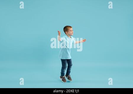 Kindheit und Traum von der großen und berühmten Zukunft. Ziemlich kleiner Junge isoliert auf blauem Studiohintergrund. Träume, Phantasie, Bildung, Gesichtsausdruck, Emotionen Konzept. Copyspace. Stockfoto