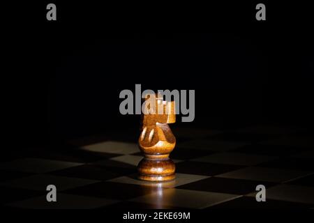 Schachfigur aus dunklem Holz an Bord mit schwarzem Hintergrund. Stockfoto