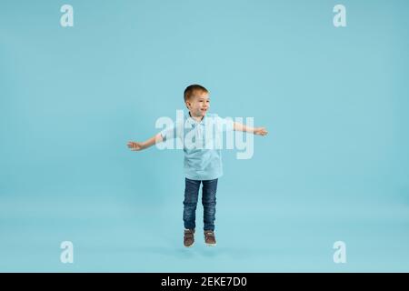 Kindheit und Traum von der großen und berühmten Zukunft. Ziemlich kleiner Junge isoliert auf blauem Studiohintergrund. Träume, Phantasie, Bildung, Gesichtsausdruck, Emotionen Konzept. Copyspace. Stockfoto