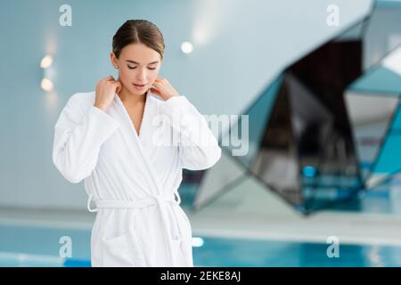 Junge Frau, die weißen Bademantel im Spa-Center anpasst Stockfoto