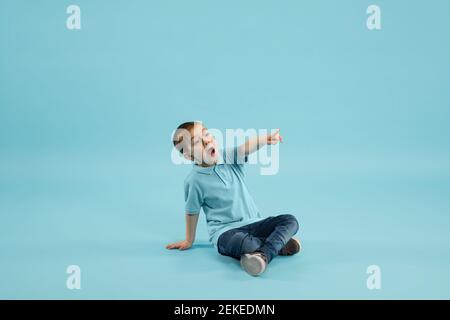 Zeigen. Kindheit und Traum von der großen und berühmten Zukunft. Ziemlich kleiner Junge isoliert auf blauem Studiohintergrund. Träume, Phantasie, Bildung, Gesichtsausdruck, Emotionen Konzept. Stockfoto