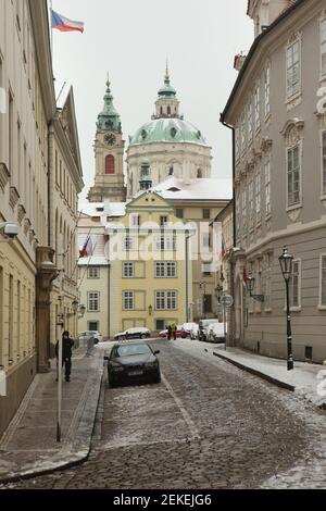 Verschneite historische Altstadt von Prag mit der Nikolaikirche (Kostel svatého Mikuláše) auf dem Malostranské-Platz, abgebildet von der Sněmovní-Straße in der Kleinseite in Prag, Tschechische Republik. Stockfoto