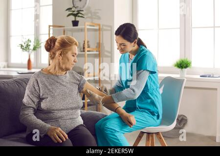 Krankenschwester gibt Arm Injektion zu pensionierten reifen Frau, die sitzt Auf der Couch zu Hause Stockfoto