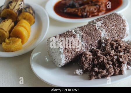 Gedämpfte Fingerhirse und Kokosnusskuchen, serviert mit Sardinen-Curry und gedämpfter Kochbanane. Schuss auf weißem Untergrund Stockfoto