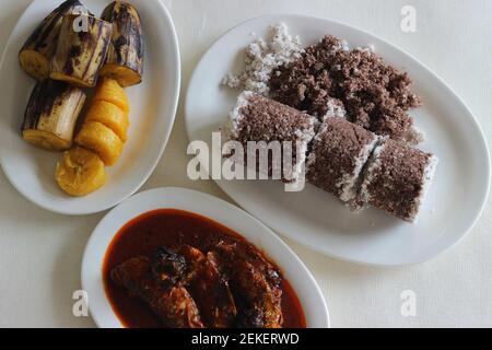 Gedämpfte Fingerhirse und Kokosnusskuchen, serviert mit Sardinen-Curry und gedämpfter Kochbanane. Schuss auf weißem Untergrund Stockfoto