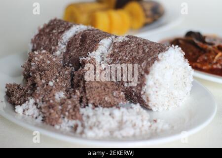 Gedämpfte Fingerhirse und Kokosnusskuchen, serviert mit Sardinen-Curry und gedämpfter Kochbanane. Schuss auf weißem Untergrund Stockfoto