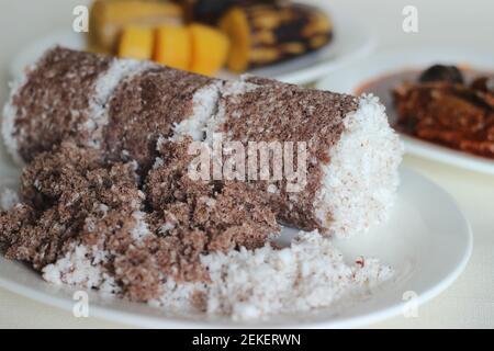 Gedämpfte Fingerhirse und Kokosnusskuchen, serviert mit Sardinen-Curry und gedämpfter Kochbanane. Schuss auf weißem Untergrund Stockfoto