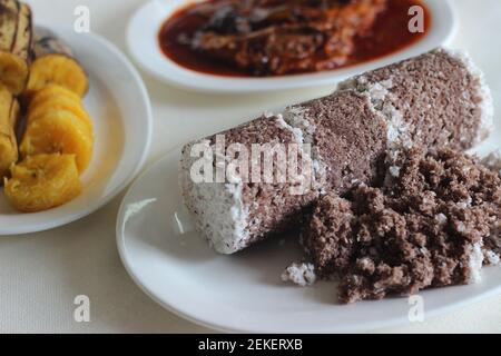 Gedämpfte Fingerhirse und Kokosnusskuchen, serviert mit Sardinen-Curry und gedämpfter Kochbanane. Schuss auf weißem Untergrund Stockfoto