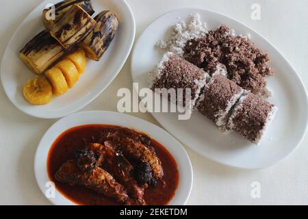 Gedämpfte Fingerhirse und Kokosnusskuchen, serviert mit Sardinen-Curry und gedämpfter Kochbanane. Schuss auf weißem Untergrund Stockfoto